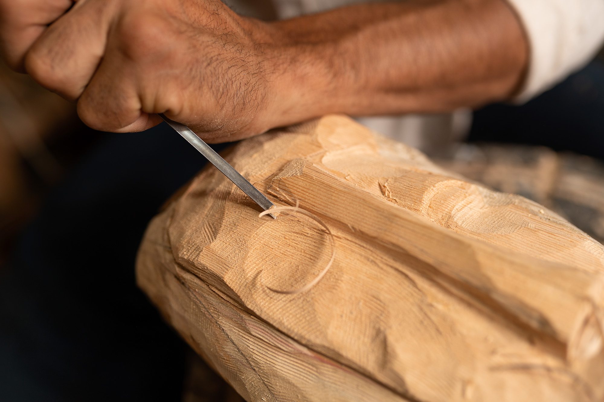 Main d’un artisan sculptant le bois au ciseau, un copeau s’enroule sous la lame