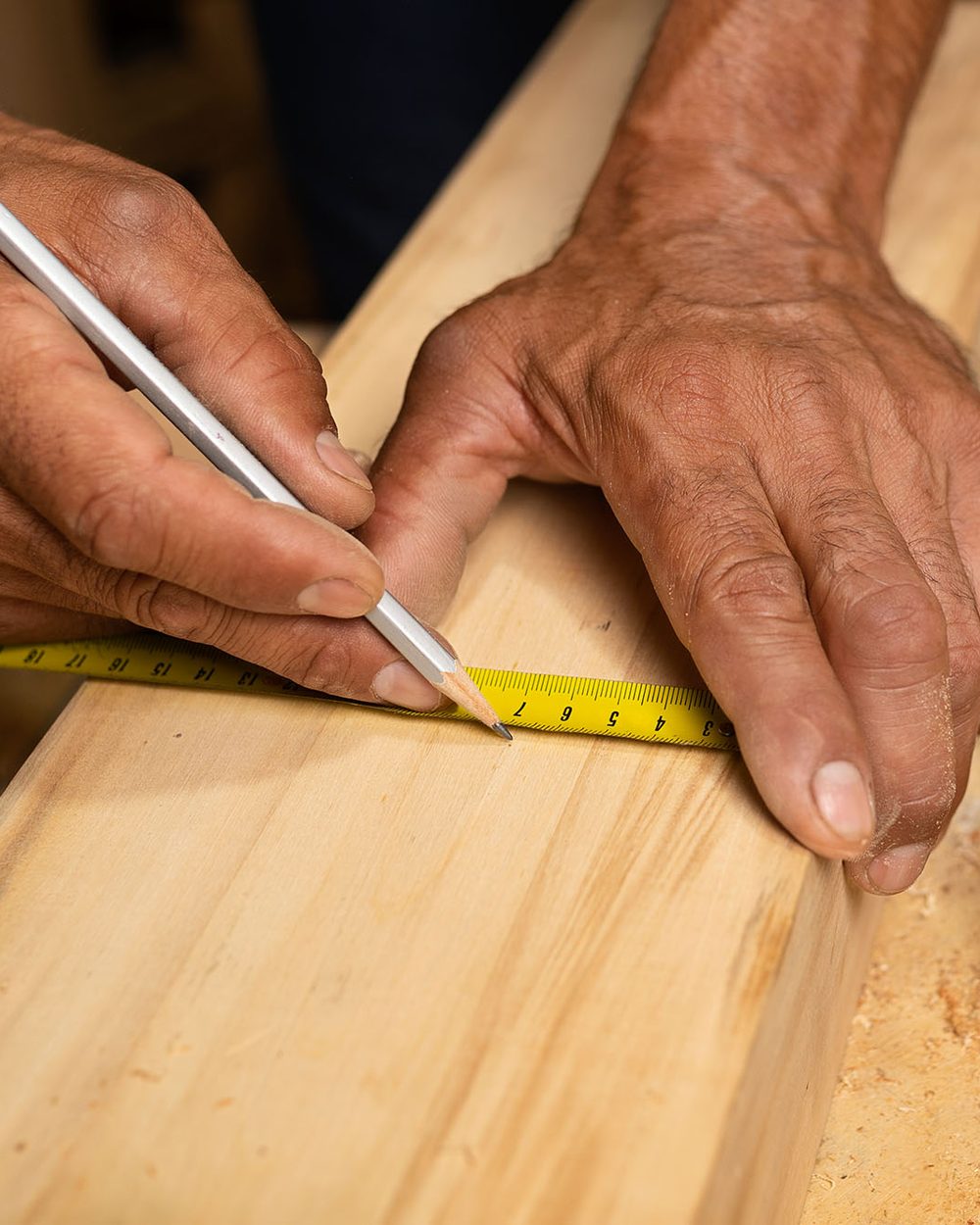 Mains d’un menuisier traçant une mesure au crayon sur une planche de bois
